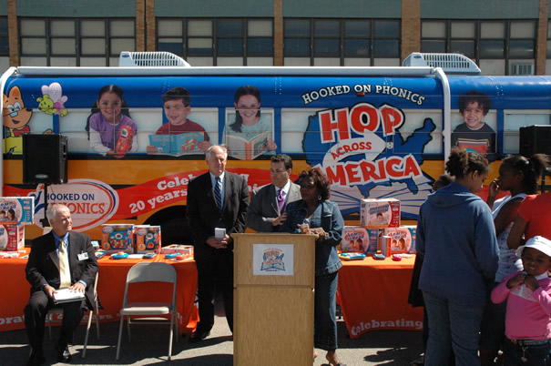 Above photo: Illinois Lieutenant Governor Pat Quinn (second from left) read a proclamation declaring “Hooked on Phonics Week” in Illinois. The controversial program used Chicago’s all-black Crispus Attucks Elementary School (background above) and its parents, students, and teachers to help promote the program. Despite the lurch at diversity, Hooked on Phonics did not even bother to change the children depicted on its bus. The main black employees from Hooked on Phonics at the August 30 event were heavily armed security (see bottom right) who refused to answer reporters’ questions as to why so many had been deployed to protect a truckload of materials and an events bus. Substance photos by George N. Schmidt.